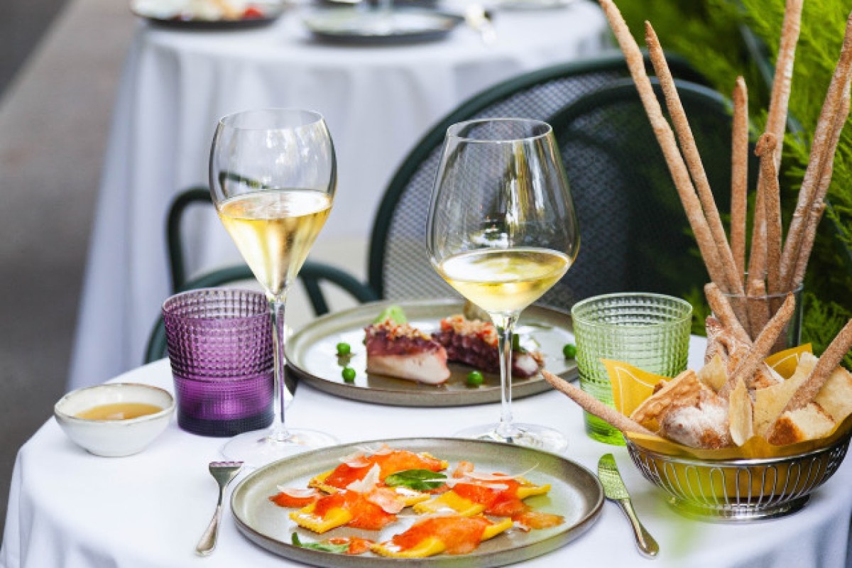 Outdoor terrace table set with wine glasses, bread sticks, octopus and ravioli dishes.