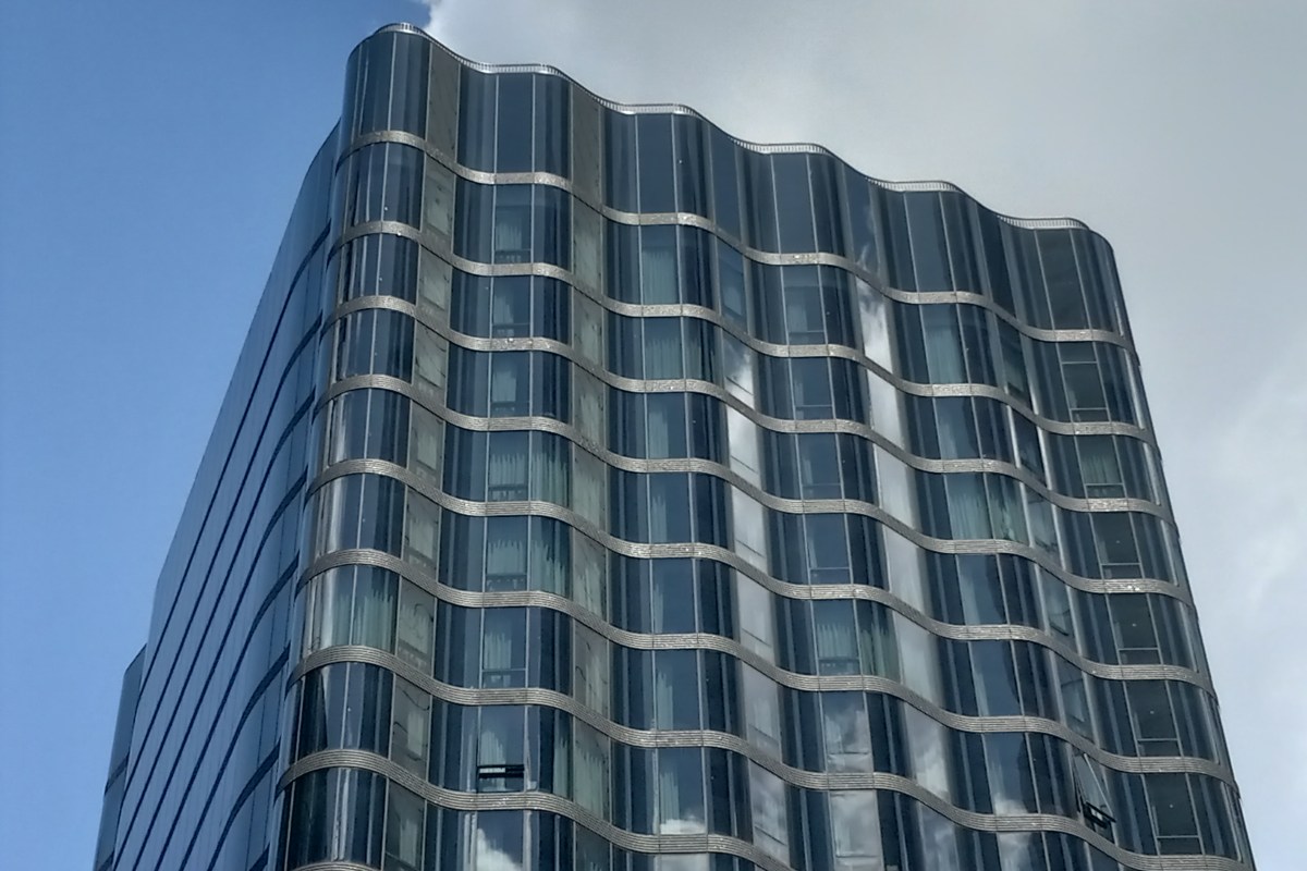 Upward view of the curved glass façade and top of Pendry Manhattan West against a cloudy sky