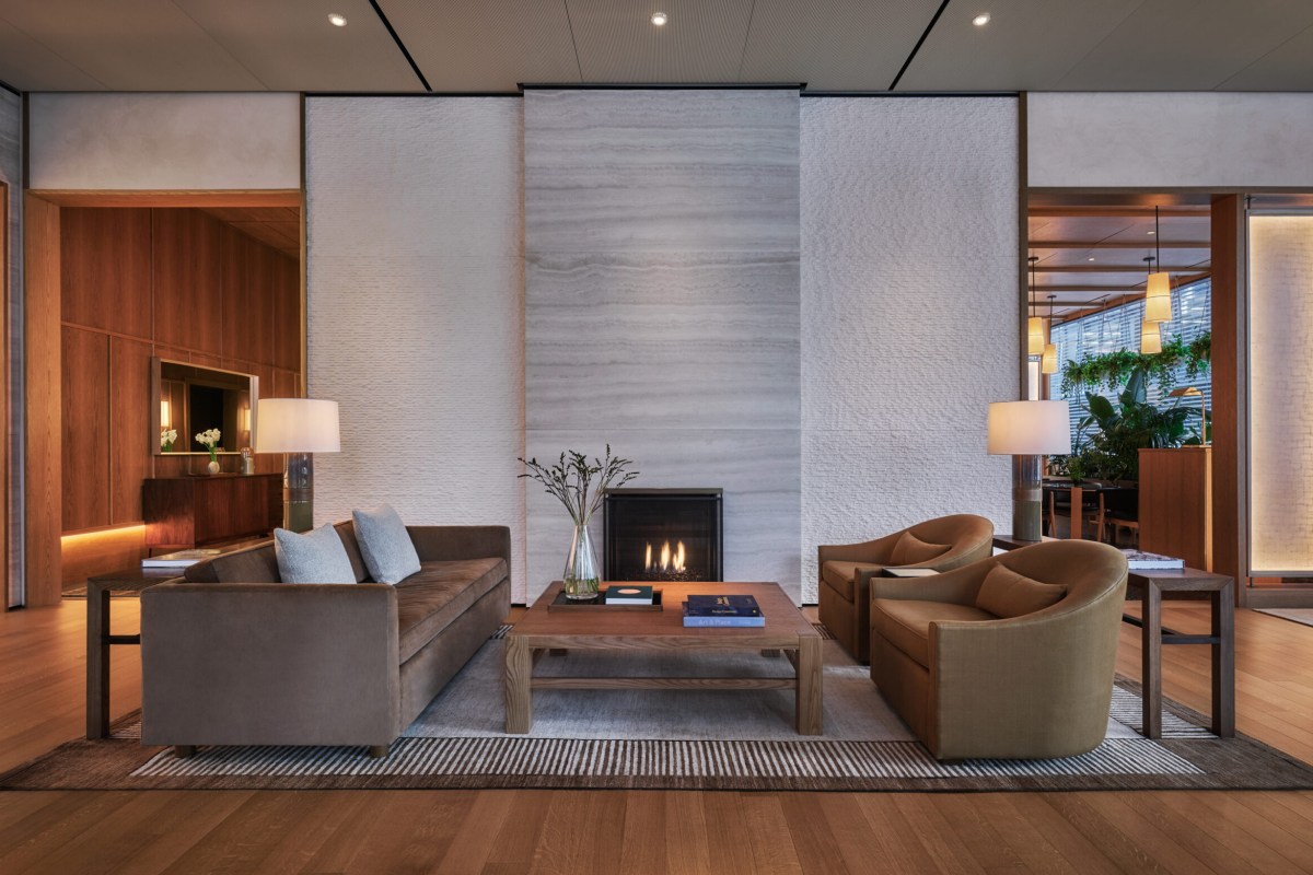 Hotel lobby lounge with stone fireplace, velvet sofa, and warm wood floors