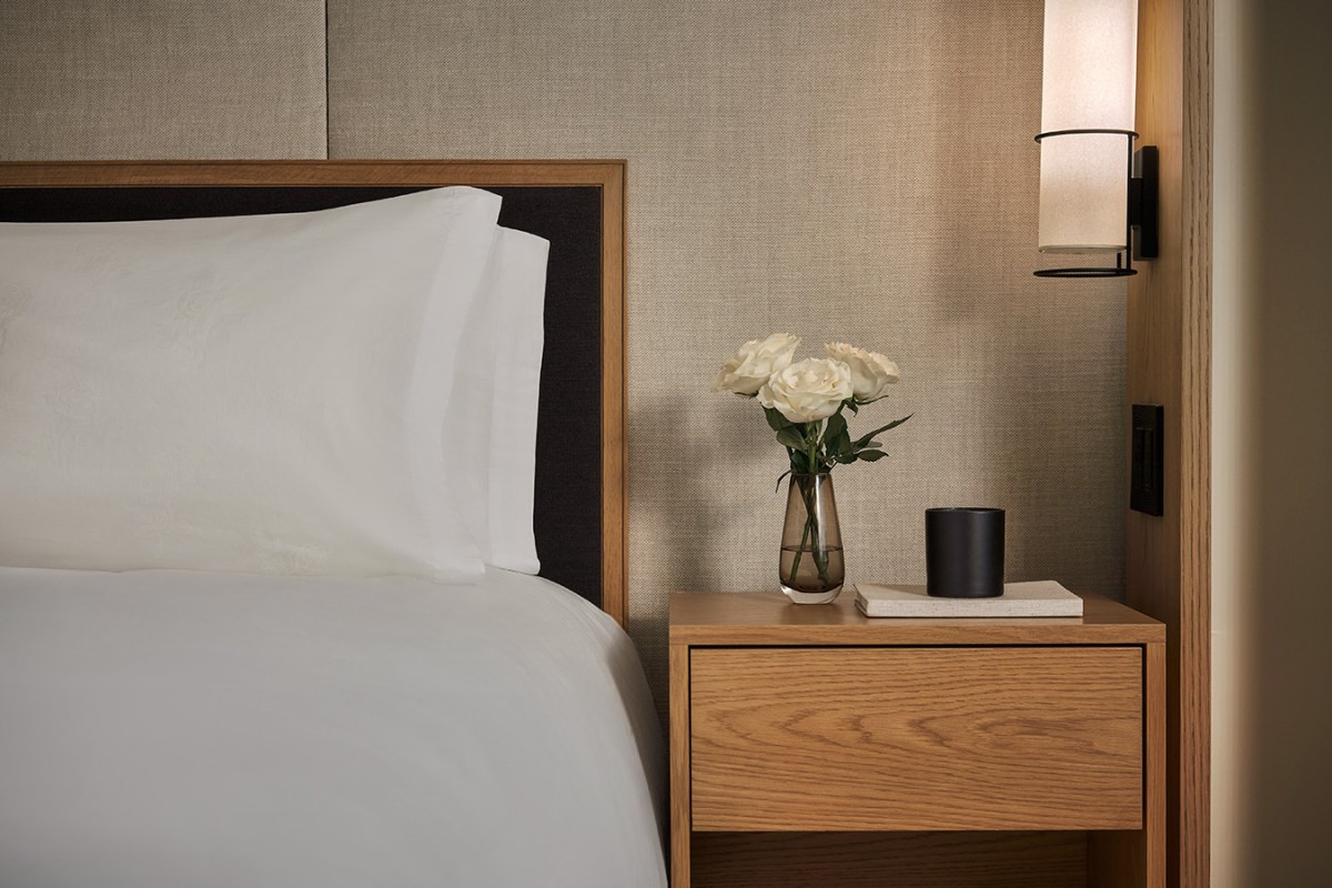 Bedside detail with fresh roses, candle, and wood nightstand in guest room