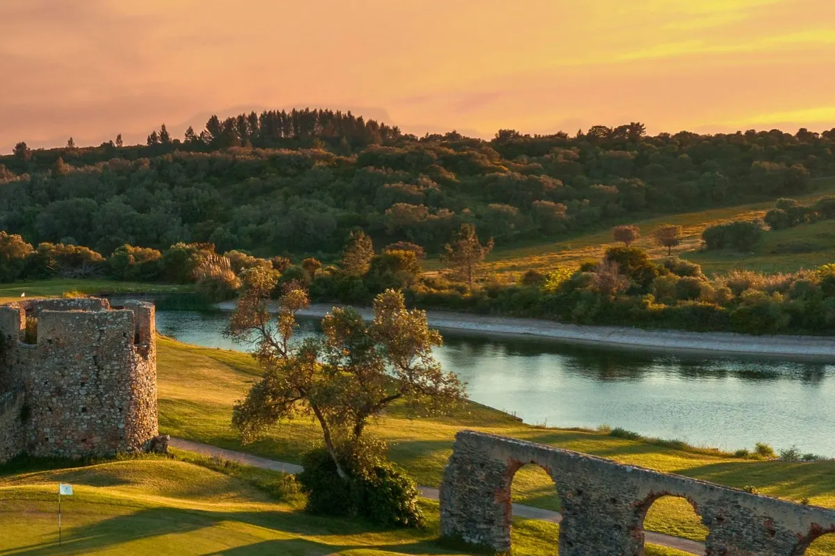 Golden sunset view of ancient stone aqueduct and tower ruins beside a lake on the resort grounds