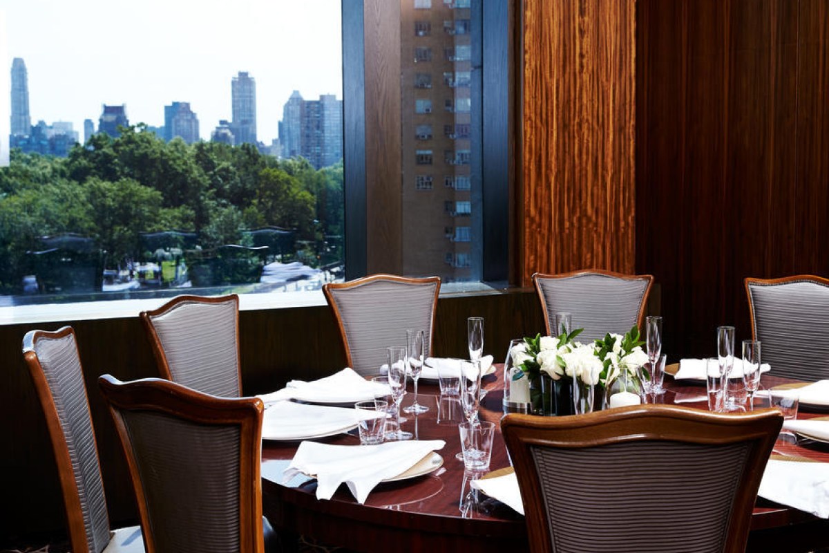 Per Se private dining room table set with white linens, overlooking Central Park skyline through window