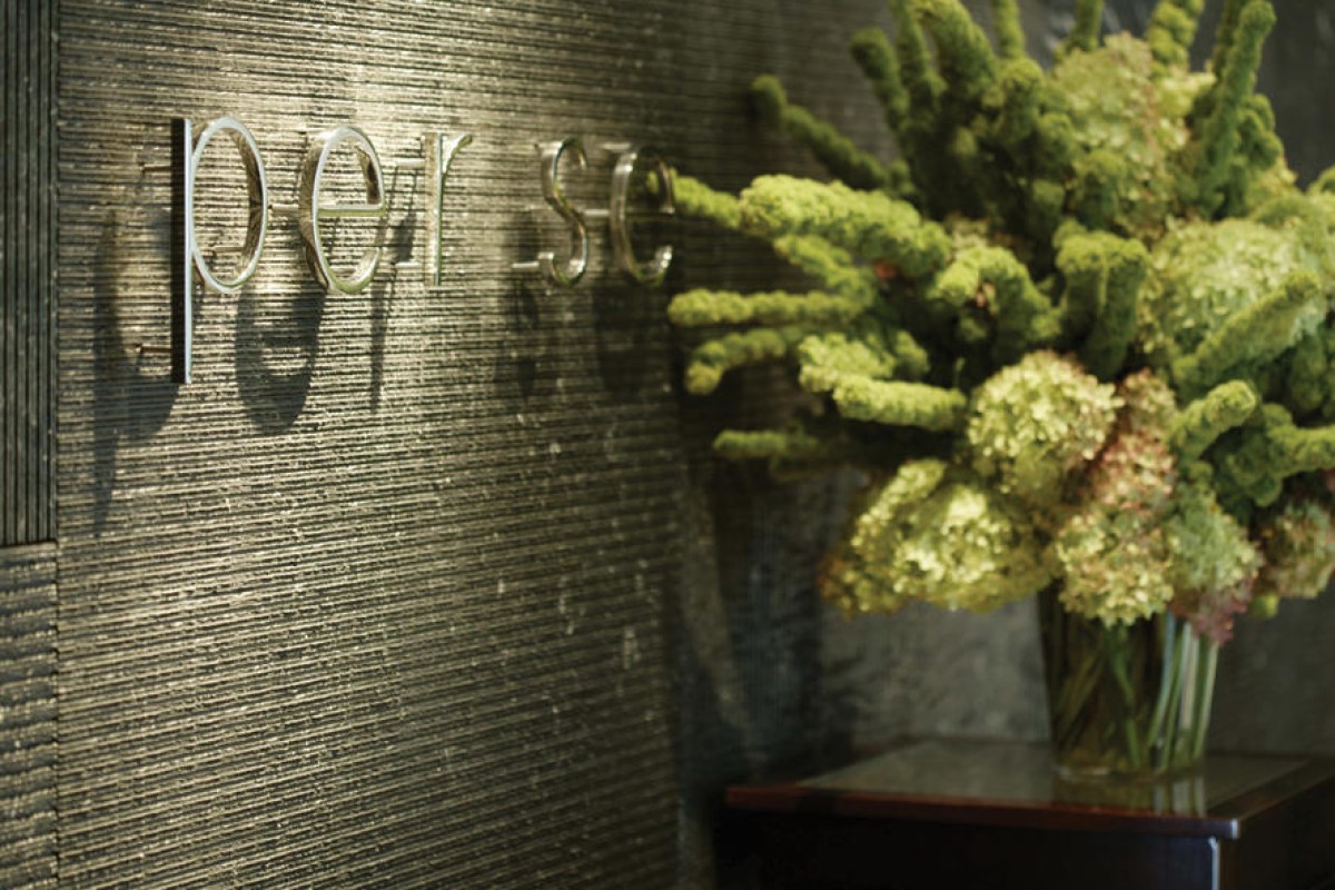 Close-up of 'per se' sign on textured wall next to a vase of green hydrangea flowers