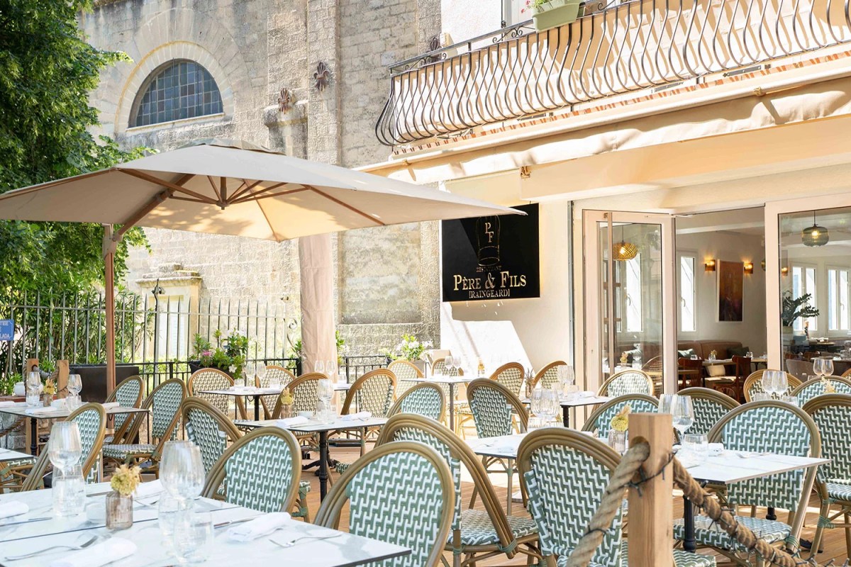 Restaurant terrace with tables, chairs, umbrella, and Père & Fils Raingeard sign on stone building facade