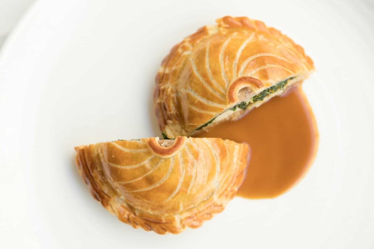 Pastry-wrapped pâté cut in half with glossy brown sauce on white plate