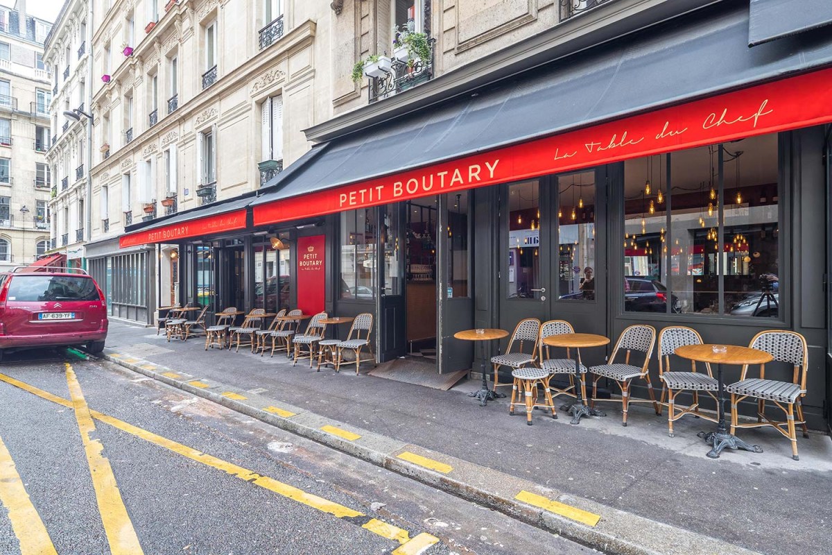 Exterior storefront of Petit Boutary with red awning, terrace tables and chairs on sidewalk