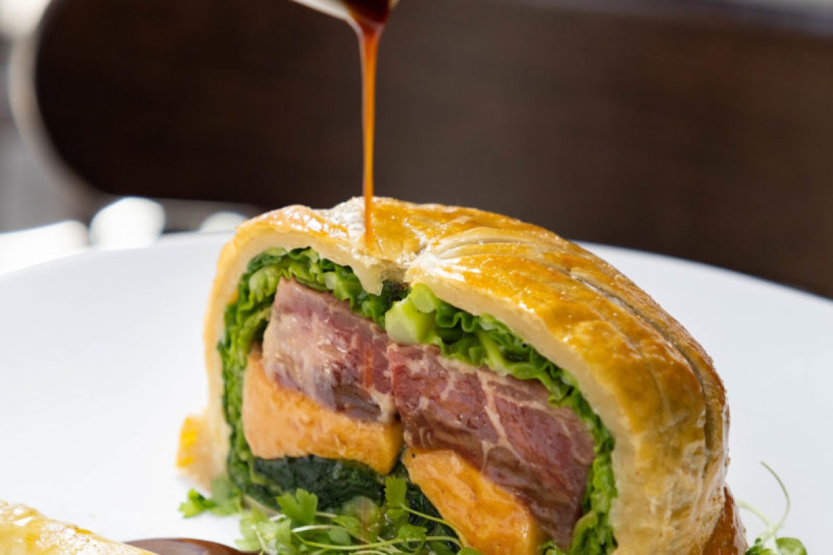 Cross-section of a meat and vegetable wellington dish with sauce being poured