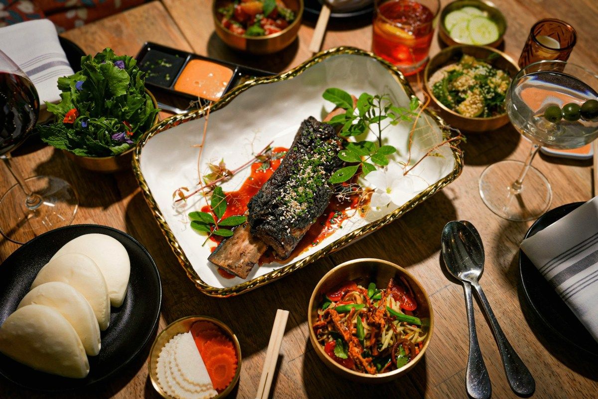Overhead shot of a wooden table spread with Asian-fusion dishes, cocktails, and wine at Phuc Yea.