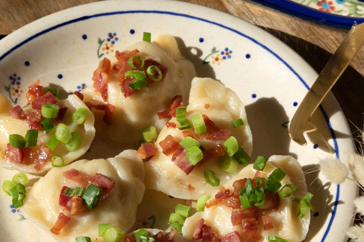 Plate of pierogi topped with bacon bits and chopped scallions on a floral-patterned dish
