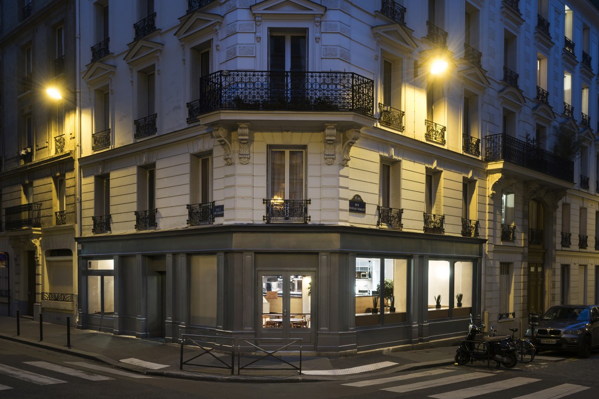 Corner building exterior at dusk, ground-floor restaurant with glowing windows on a Parisian street.