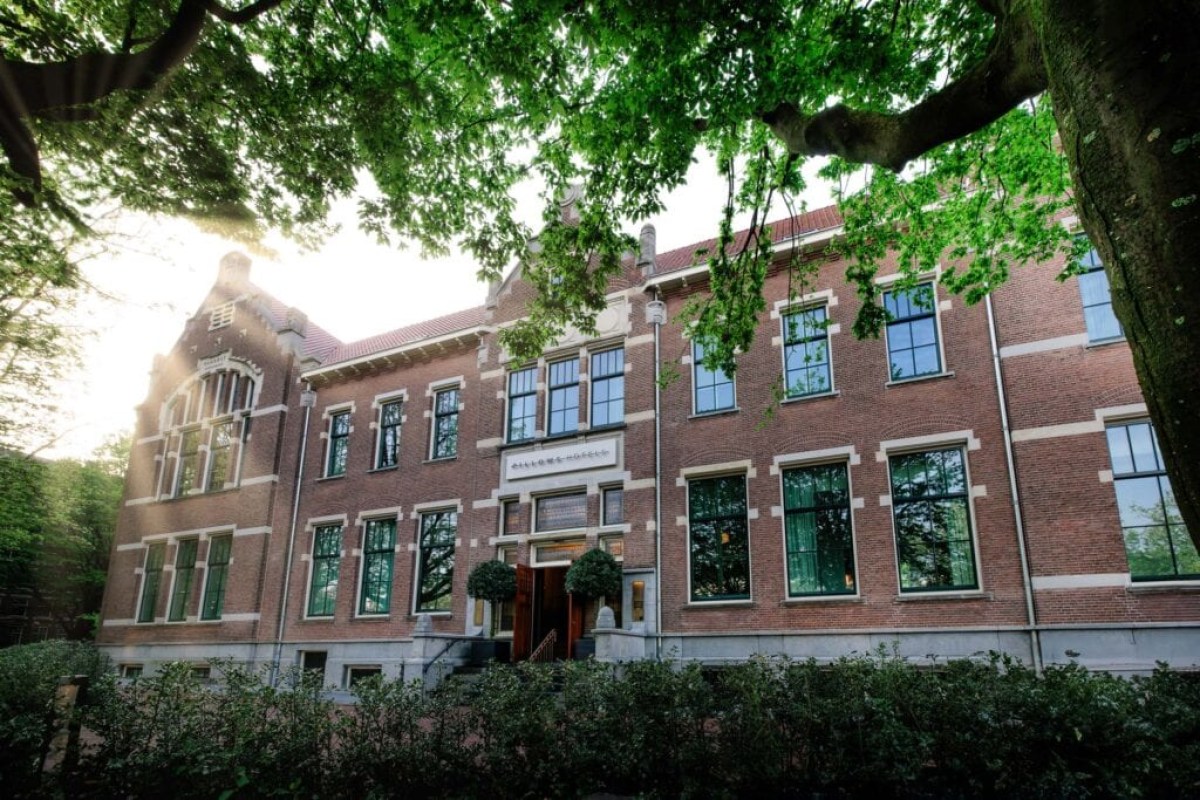 Brick facade of Pillows Grand Boutique Hotel Maurits framed by green tree branches, with entrance and tall windows visible