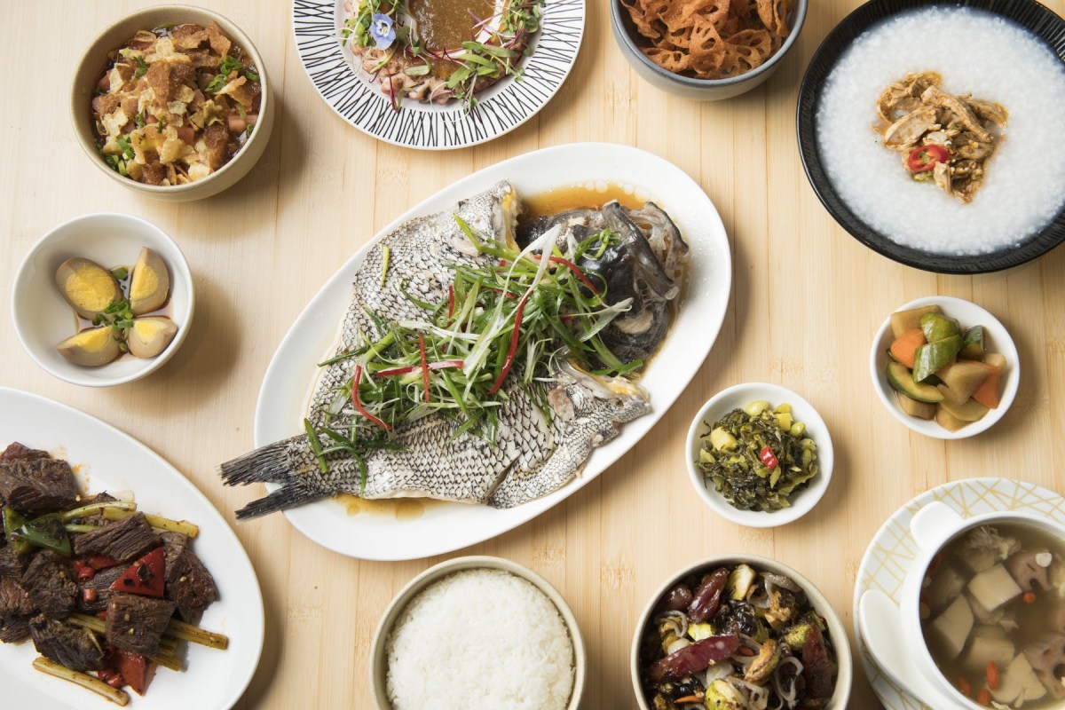 Overhead view of a Chinese feast with whole steamed fish, rice, beef skewers, congee, and side dishes on a wooden table.