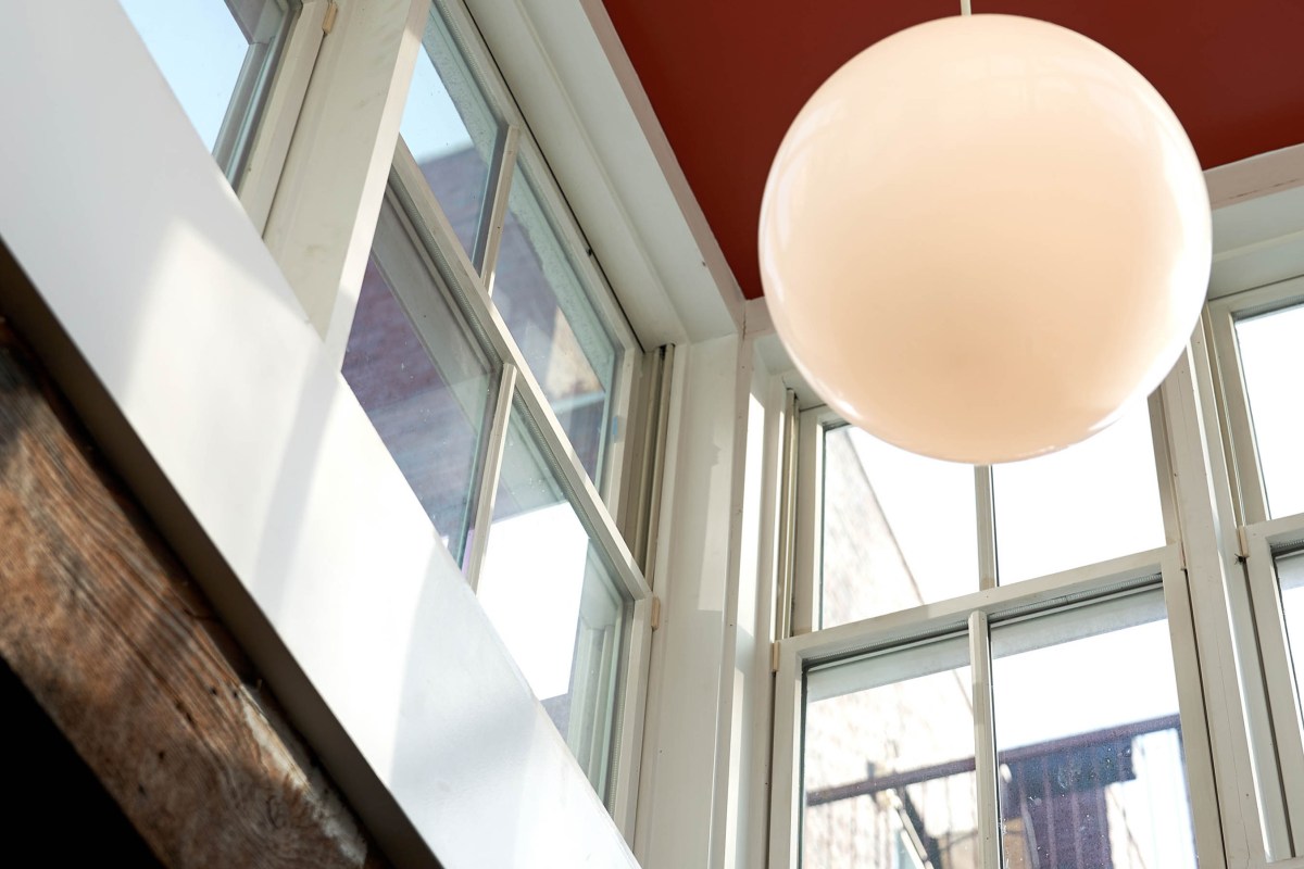 Interior detail looking up at tall windows and a round white globe pendant light against a red ceiling and wood beam