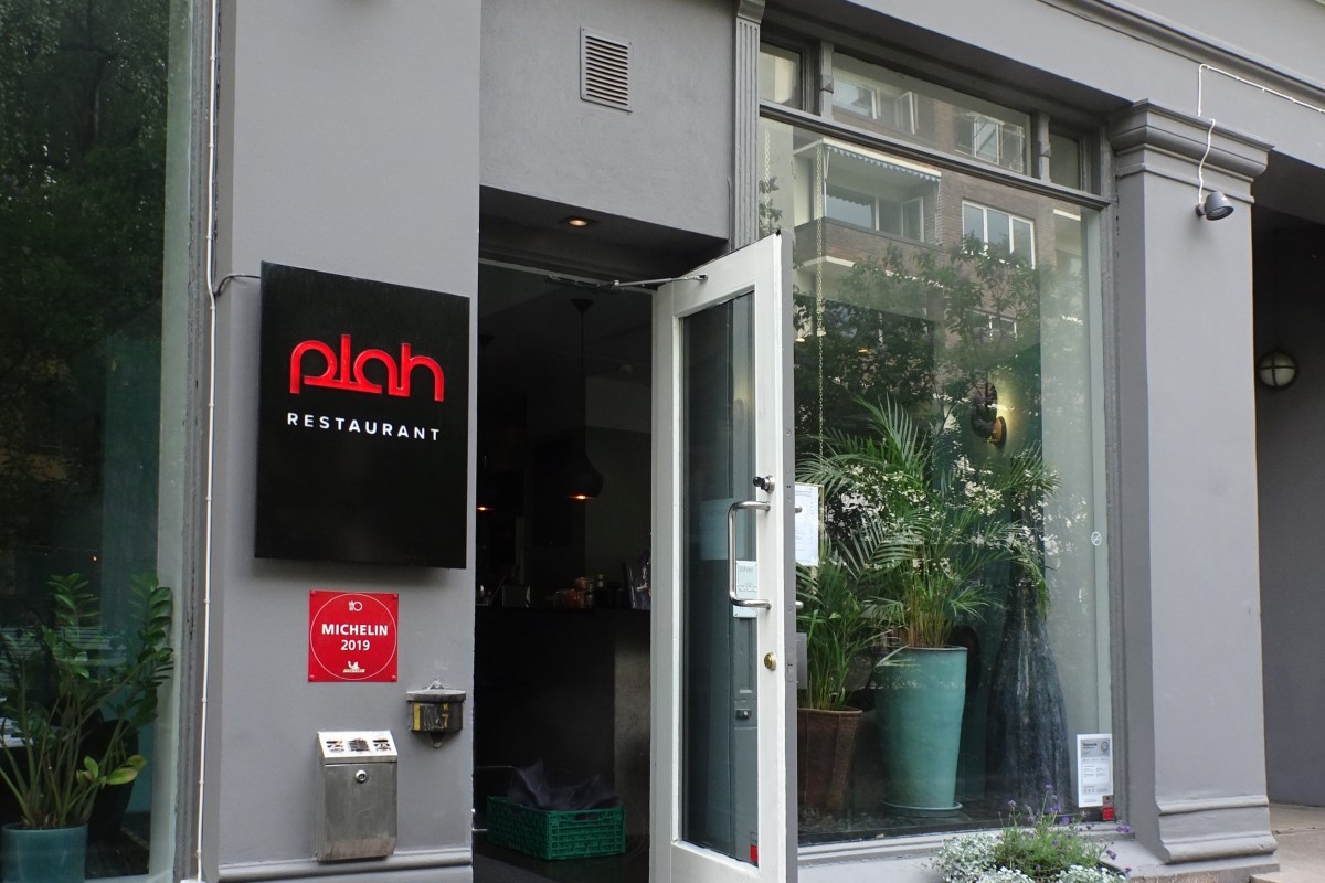 Exterior entrance of Plah restaurant with illuminated sign, open door, and plants flanking the storefront