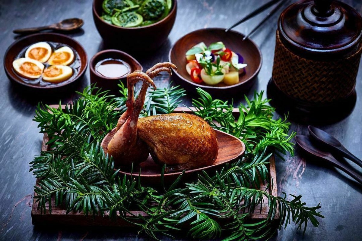 Roasted bird dish with crispy feet, served on dark wood board with greenery and side dishes of eggs, vegetables and sauce