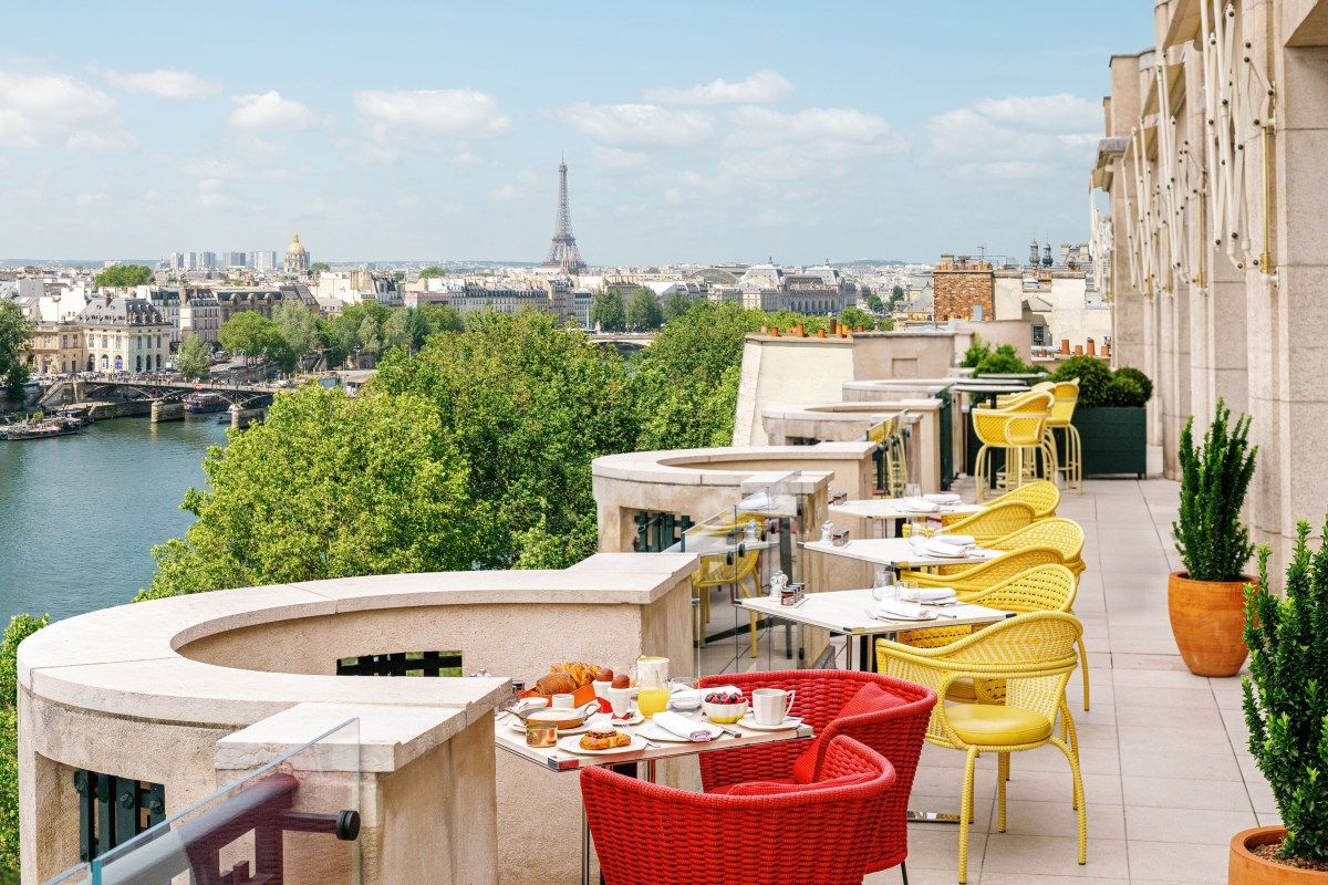 Rooftop terrace with red and yellow chairs, dining tables set, overlooking the Seine and Eiffel Tower