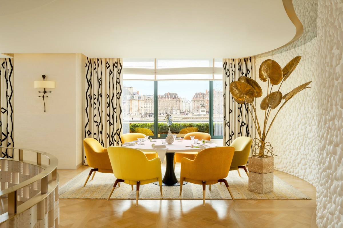 Elegant dining room with yellow armchairs around a round table, large window view of Paris rooftops