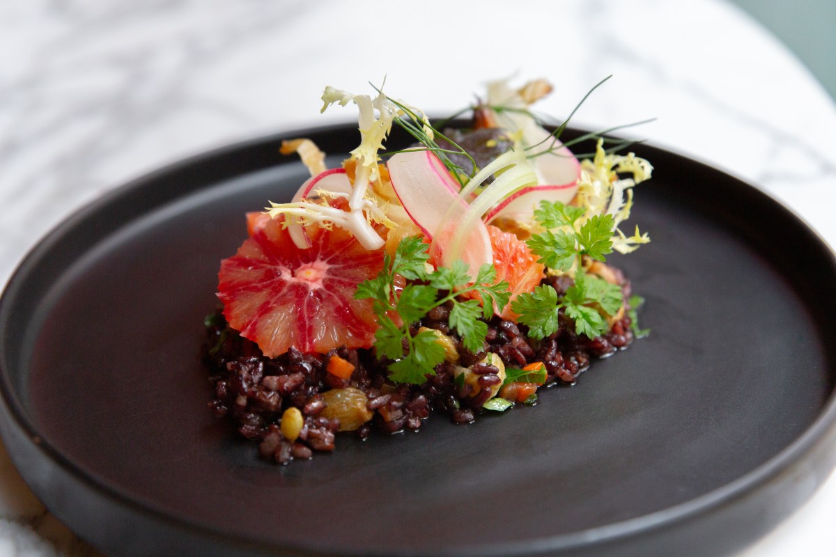 Plated dish with black rice, blood orange slices, radish, and herbs on black plate