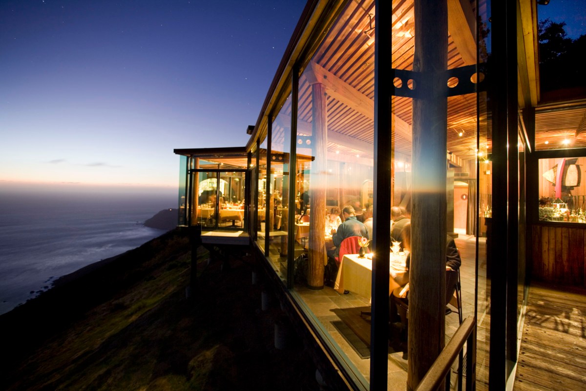 Glass-walled oceanview restaurant terrace at dusk with diners, Post Ranch Inn, Big Sur