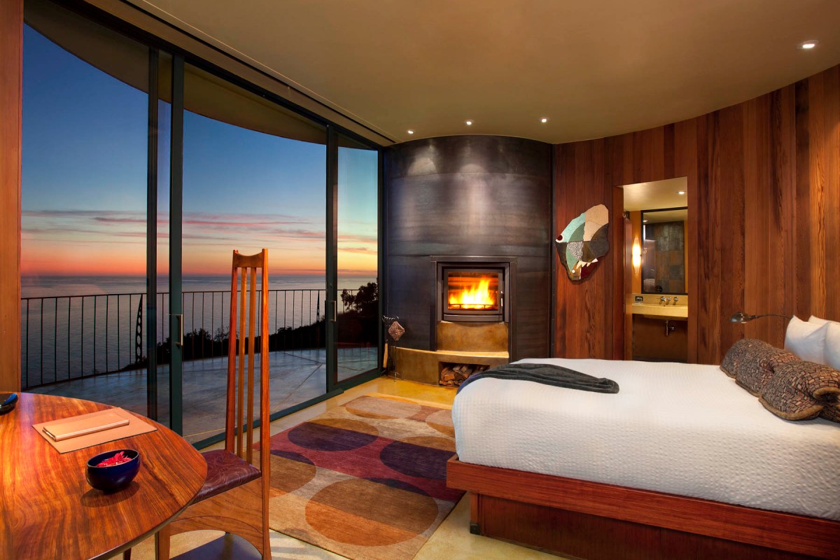 Guest room with wood paneling, lit fireplace, and panoramic ocean view at sunset