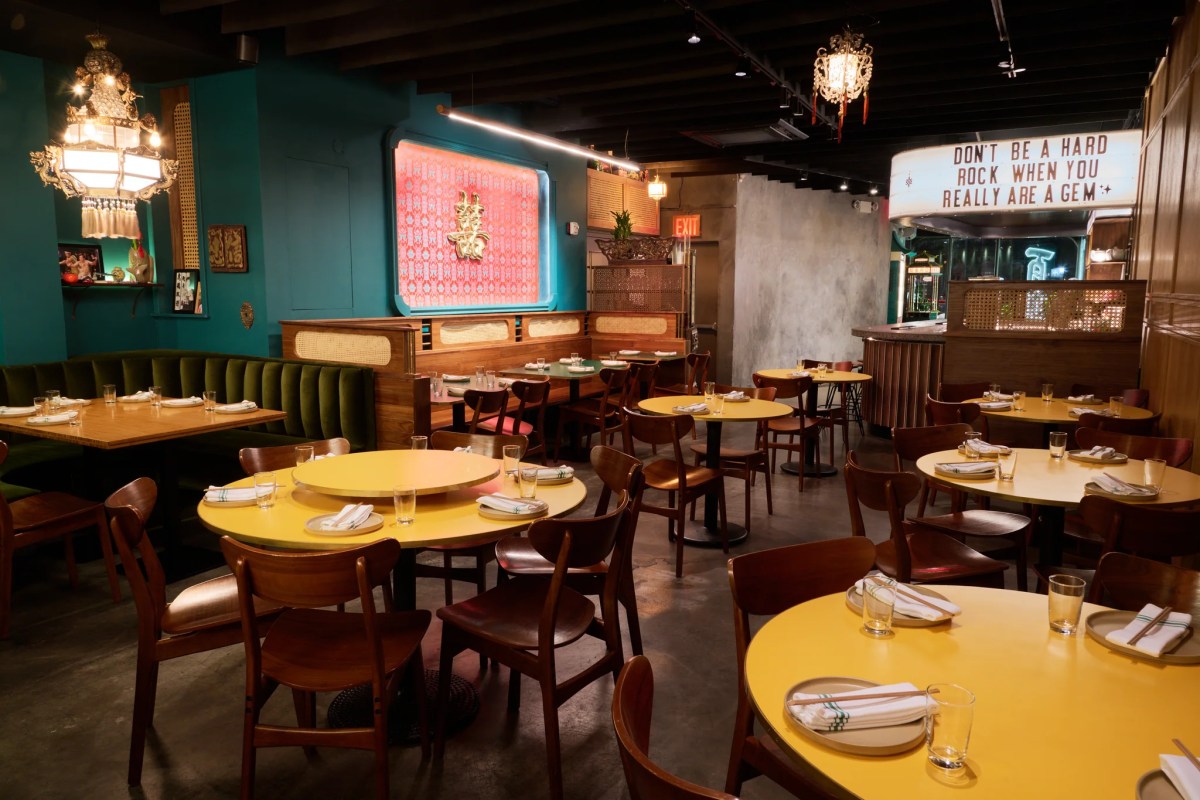 Colorful dining room with yellow round tables, teal walls, neon signage and chandeliers