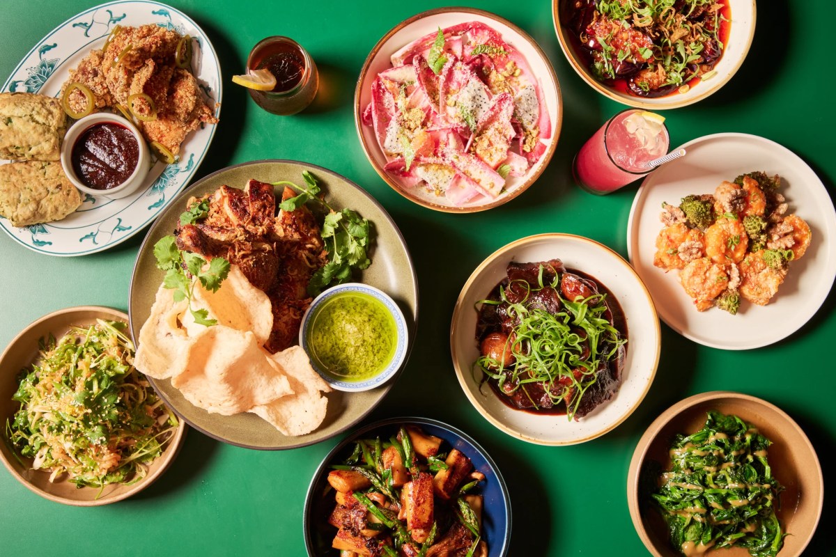 Overhead view of assorted dishes on green table including fried chicken, salads and noodles