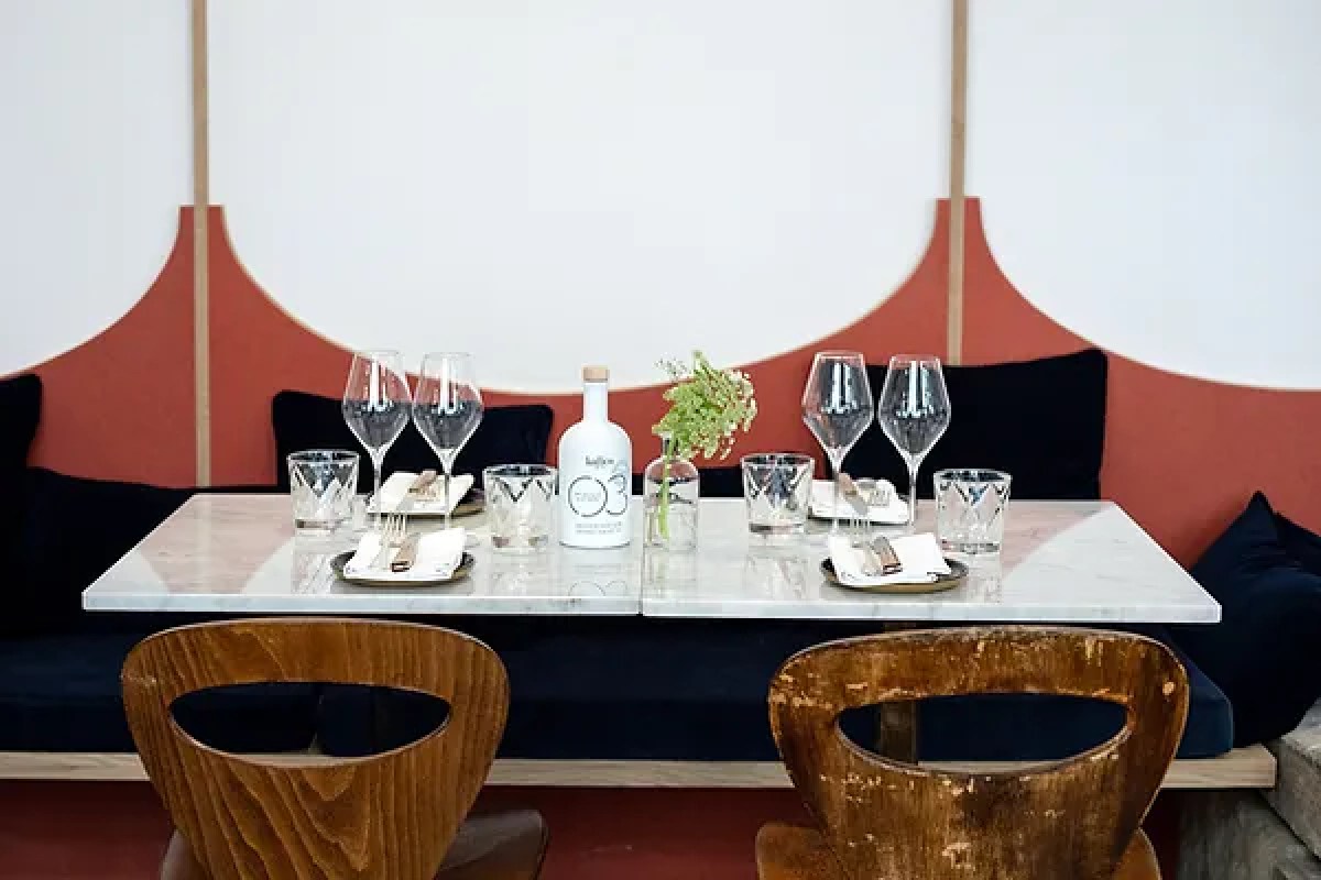 Elegant restaurant table set with wine glasses, a carafe, and a small flower vase against a terracotta and white patterned wall