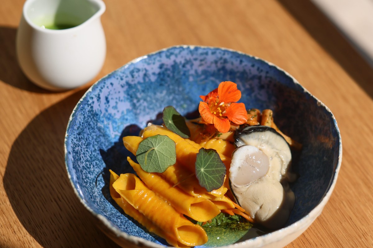 Blue ceramic bowl with orange pasta, scallop, nasturtium leaf and flower on wooden table
