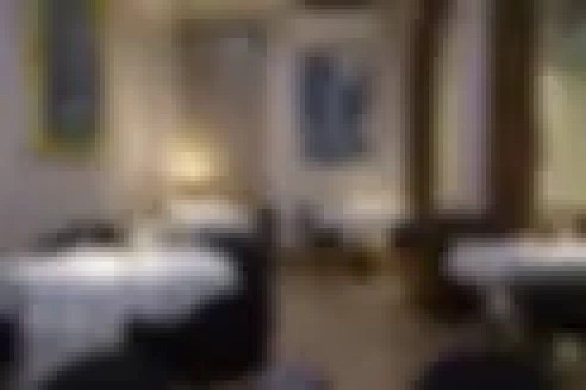 Dining room with two white-clothed tables set for service, framed blue artwork on wall