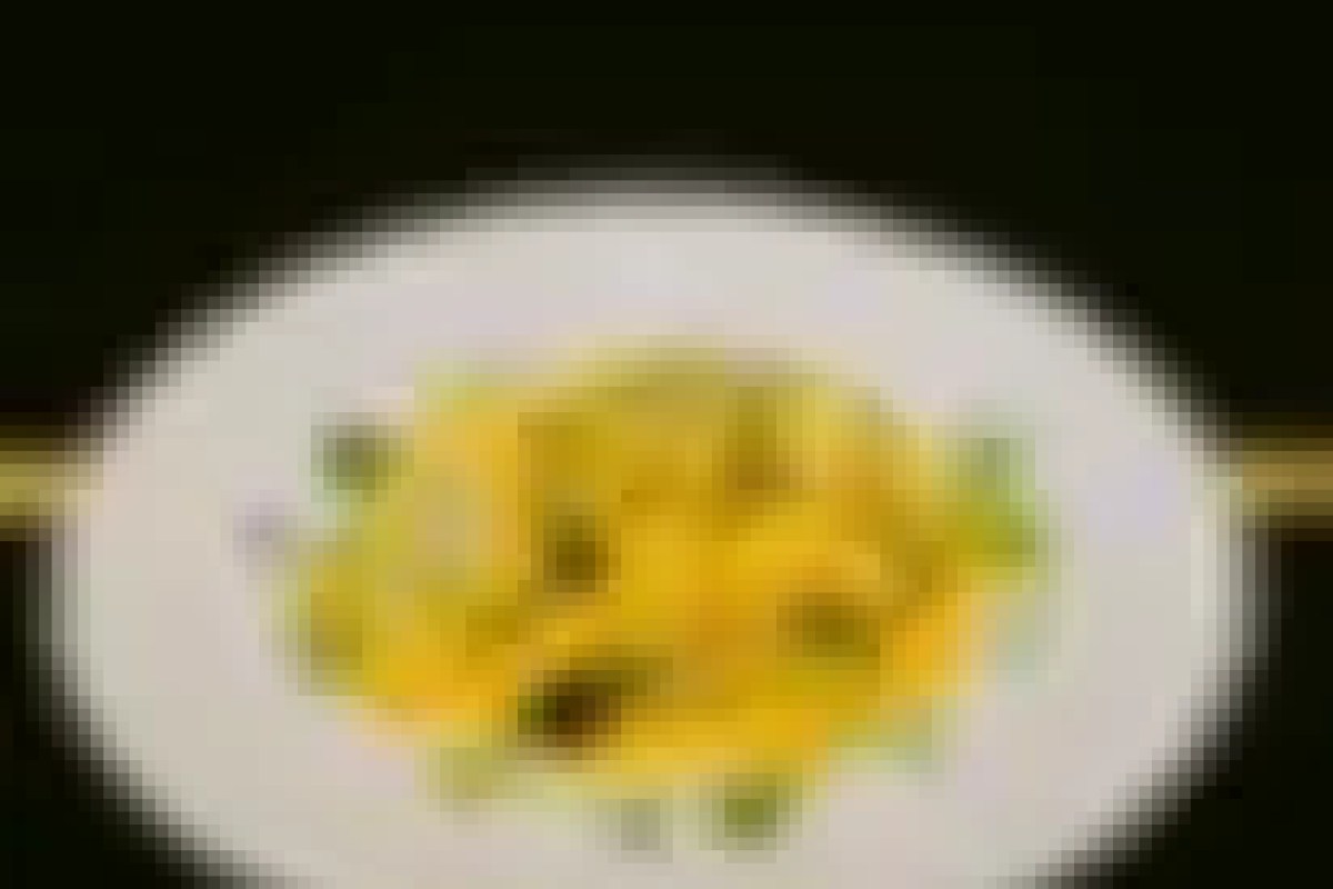 Plate of yellow pasta dish garnished with green herbs