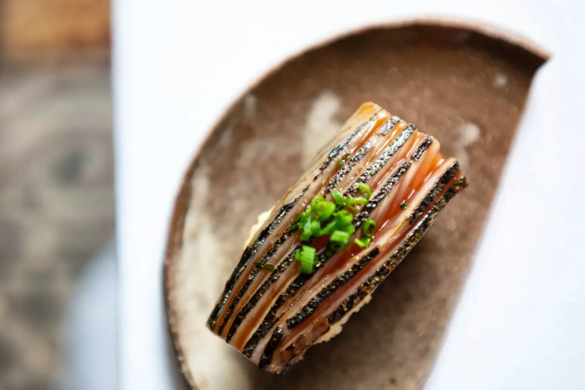 Plated dish with striped seared fish or roulade topped with chopped chives, on a dark curved ceramic plate
