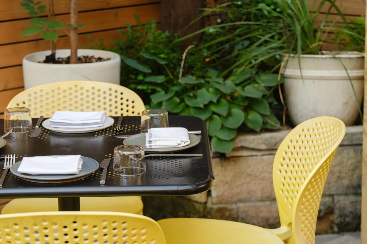 Close-up of outdoor table setting with yellow chairs and lush potted plants