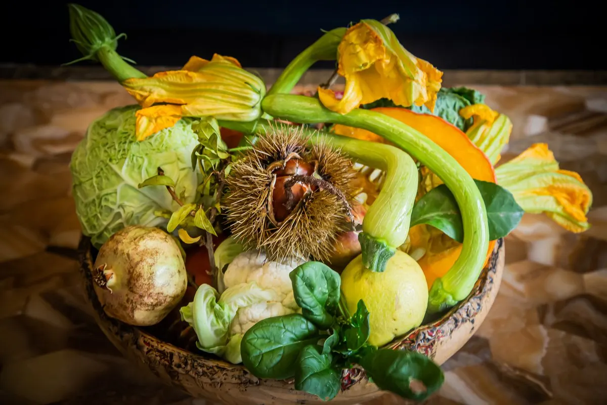 A bowl of autumn vegetables at Racines in Nice – cabbage, courgette flowers, squash, mushrooms and a chestnut burr – on a wooden table