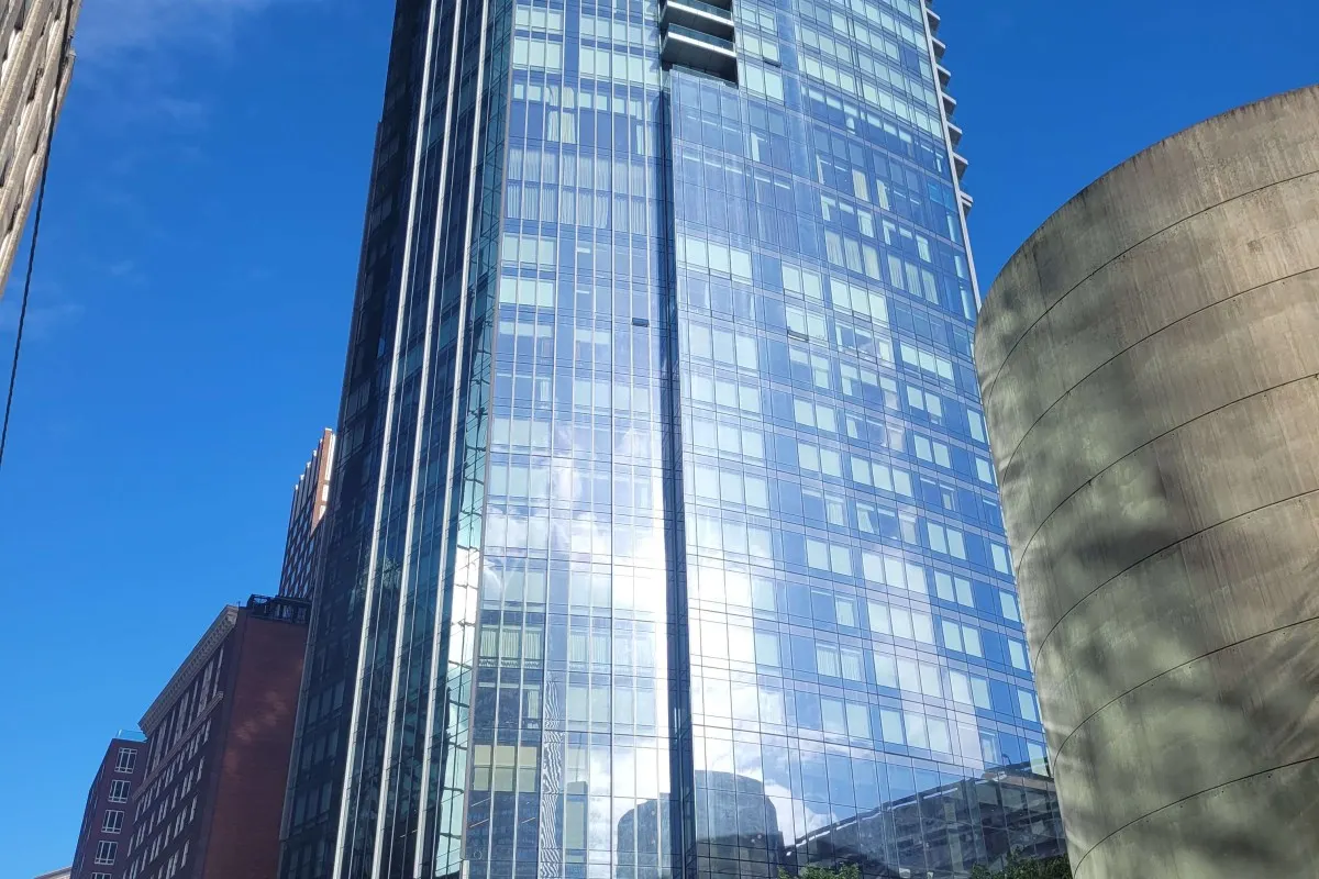 Glass high-rise tower of Raffles Boston seen from street level against a clear blue sky