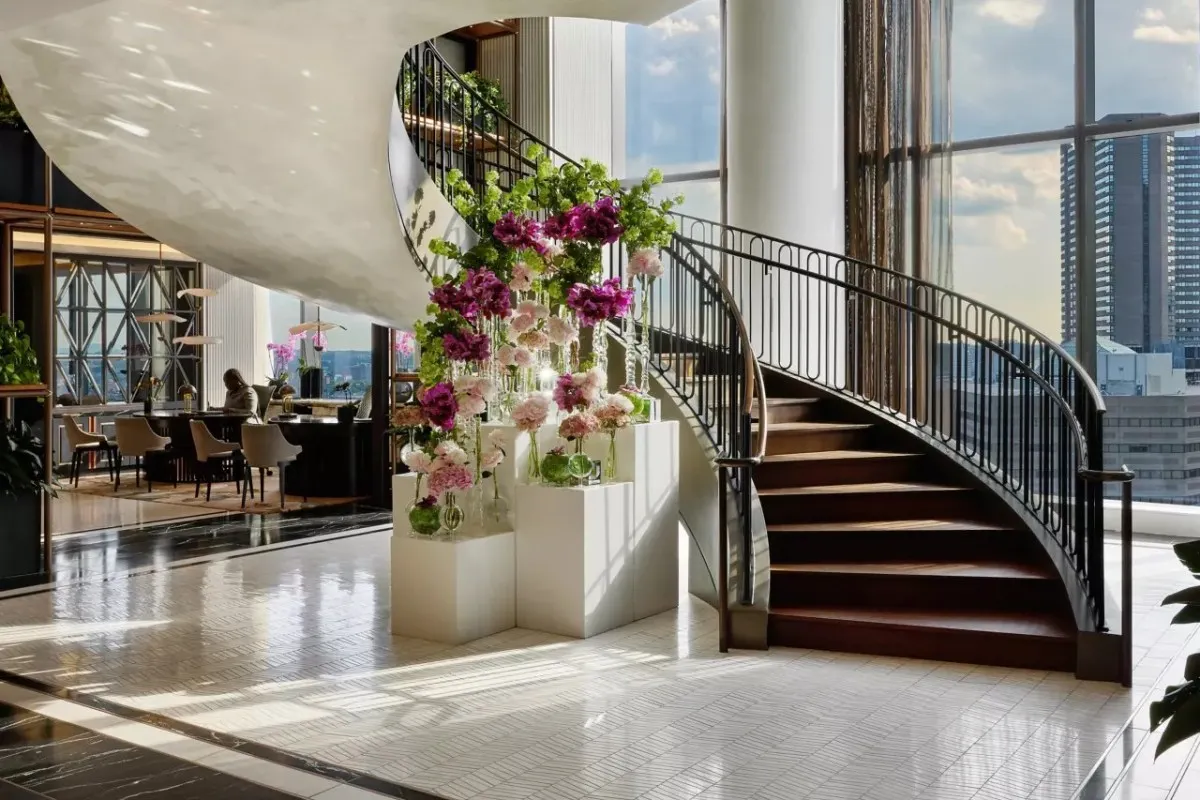 Elegant hotel lobby with spiral staircase, floral display, and city view windows