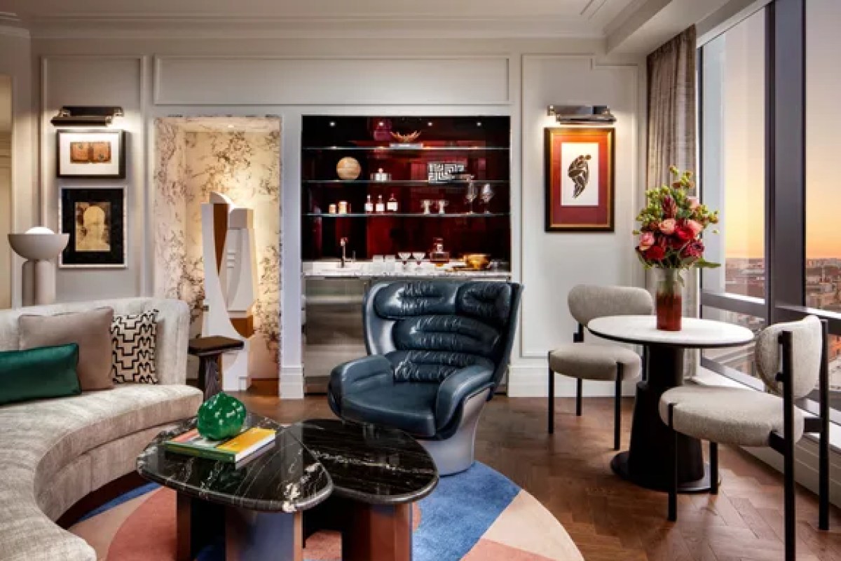 Modern hotel suite living room with blue armchair, bar nook, and city view window