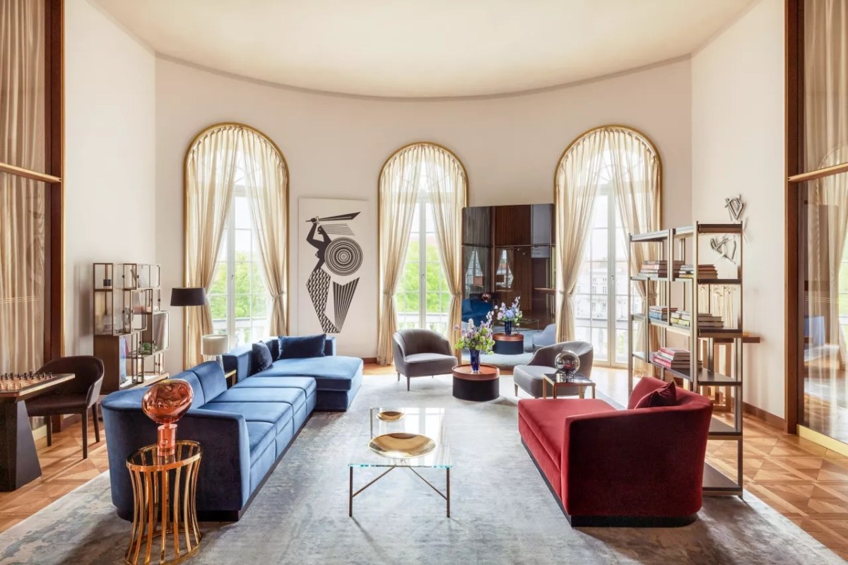Elegant hotel suite living room with blue and red velvet sofas, arched windows, and art deco decor