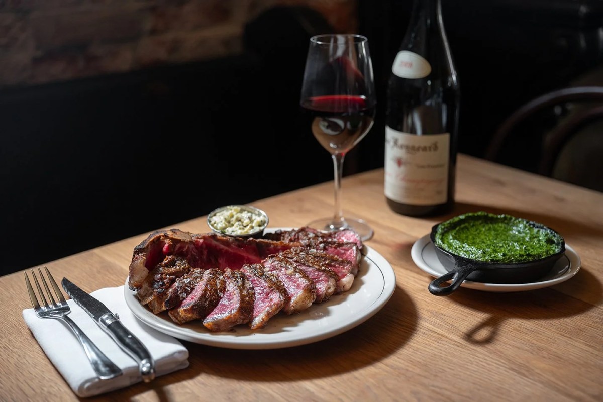 Sliced steak on white plate with creamed spinach, red wine glass and bottle on wood table