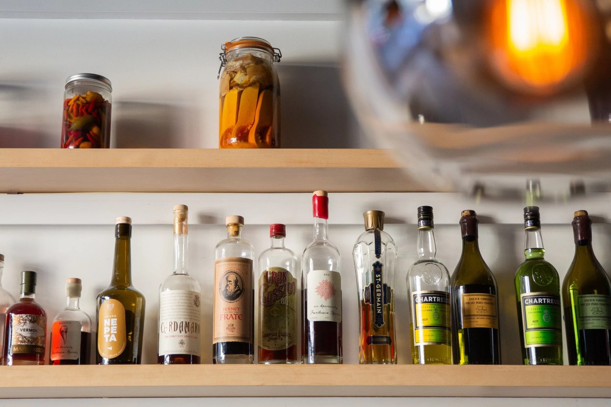 Shelf behind the bar lined with various spirit bottles and jars of infusions