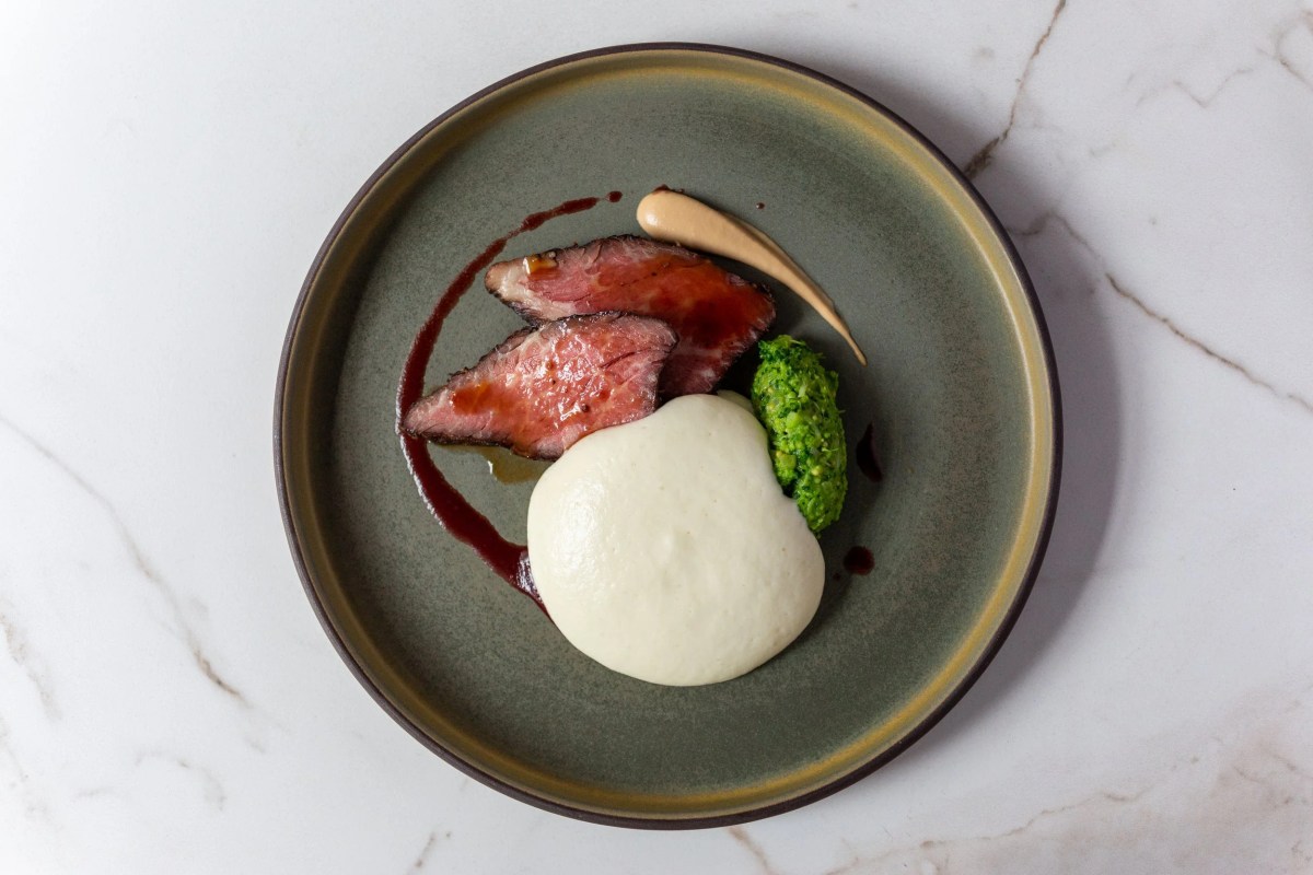 Sliced roast meat with a pea puree, herb garnish and sauce on a green plate