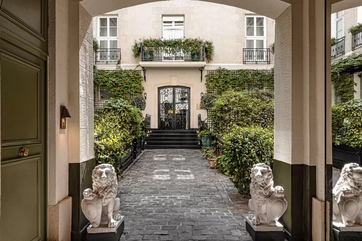 Archway view of Relais Christine's courtyard entrance with lion statues, cobblestone path, ivy-covered façade and balconies