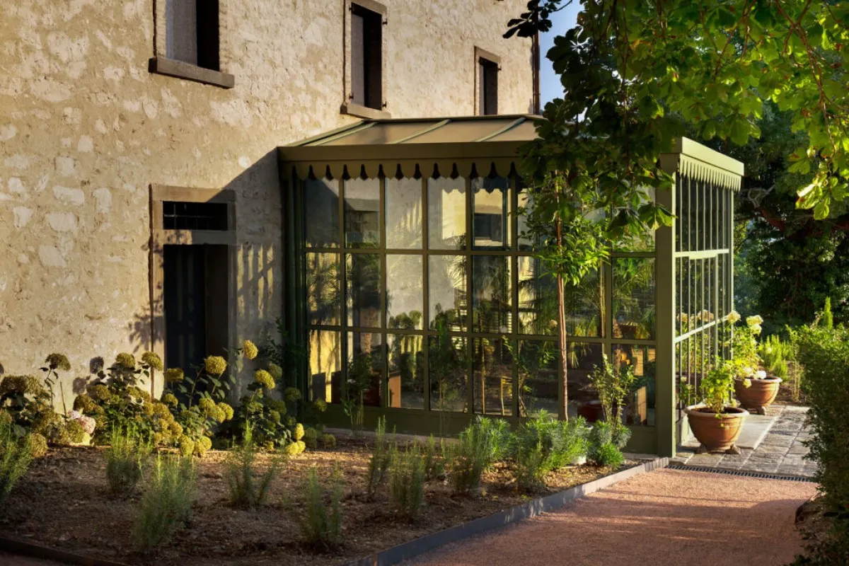 Stone hotel exterior with green-framed glass conservatory addition and lush garden