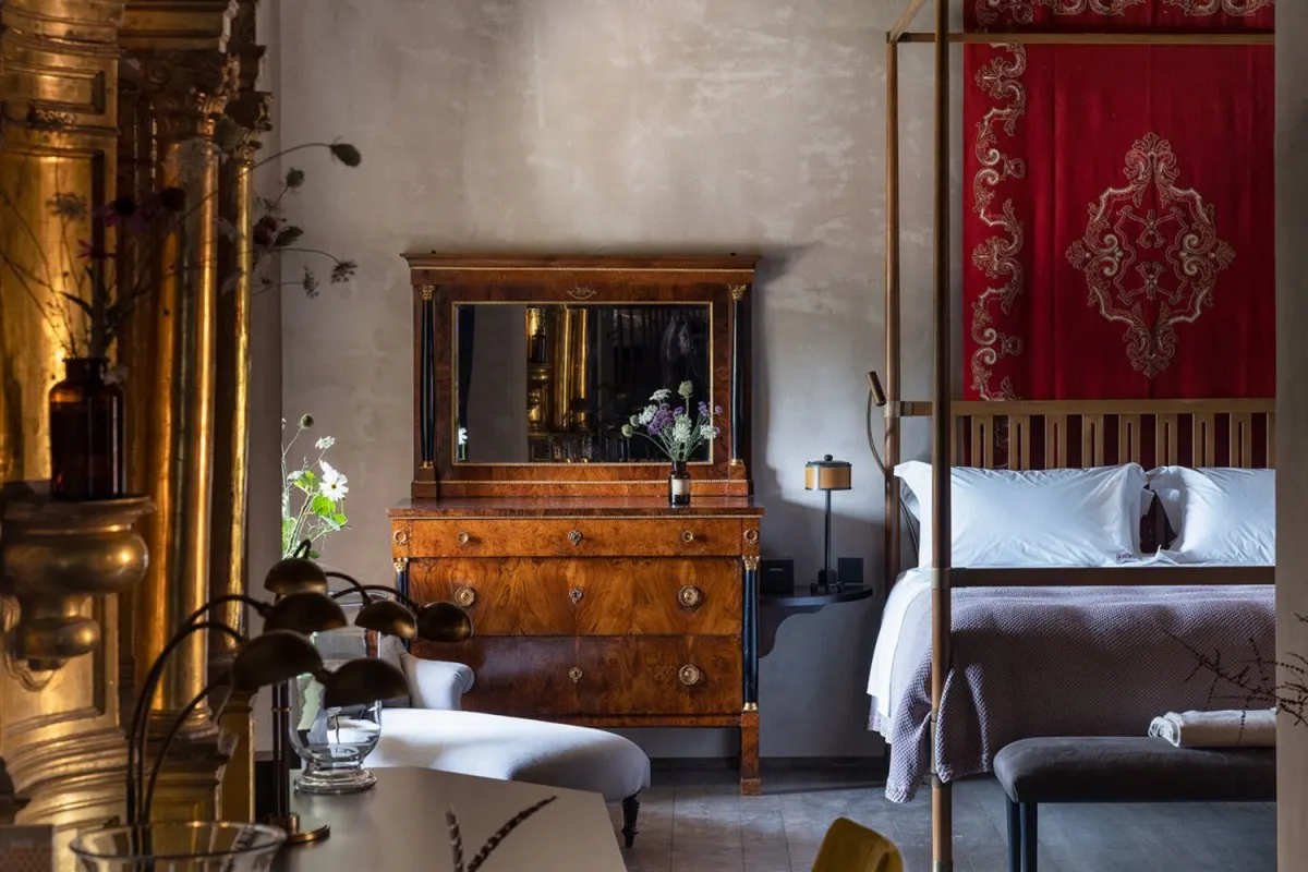 Elegant guest room with four-poster bed, red embroidered wall hanging, and antique wood dresser with mirror