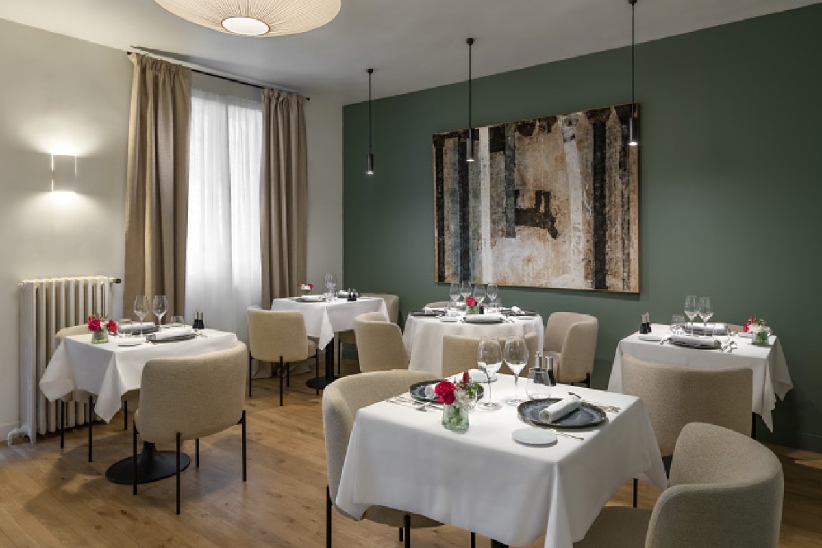 Elegant dining room with green wall, framed artwork, pendant lights, set tables with white linens