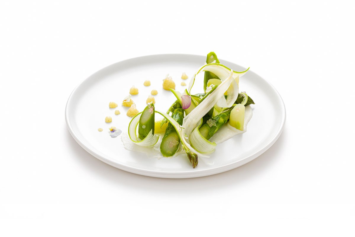 Plated dish with asparagus, thin shaved vegetable ribbons, and small garnishes on white plate