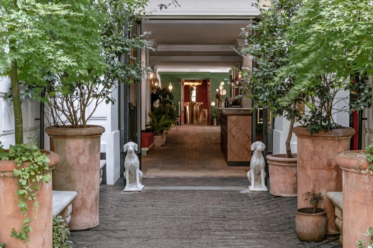 Entrance courtyard with terracotta planters, dog statues, leading into the restaurant's green-toned dining area.