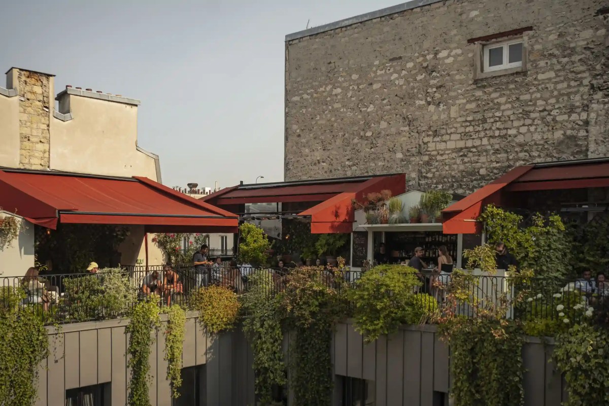 Rooftop terrace with red awnings, greenery, and guests seated at tables in late afternoon light.