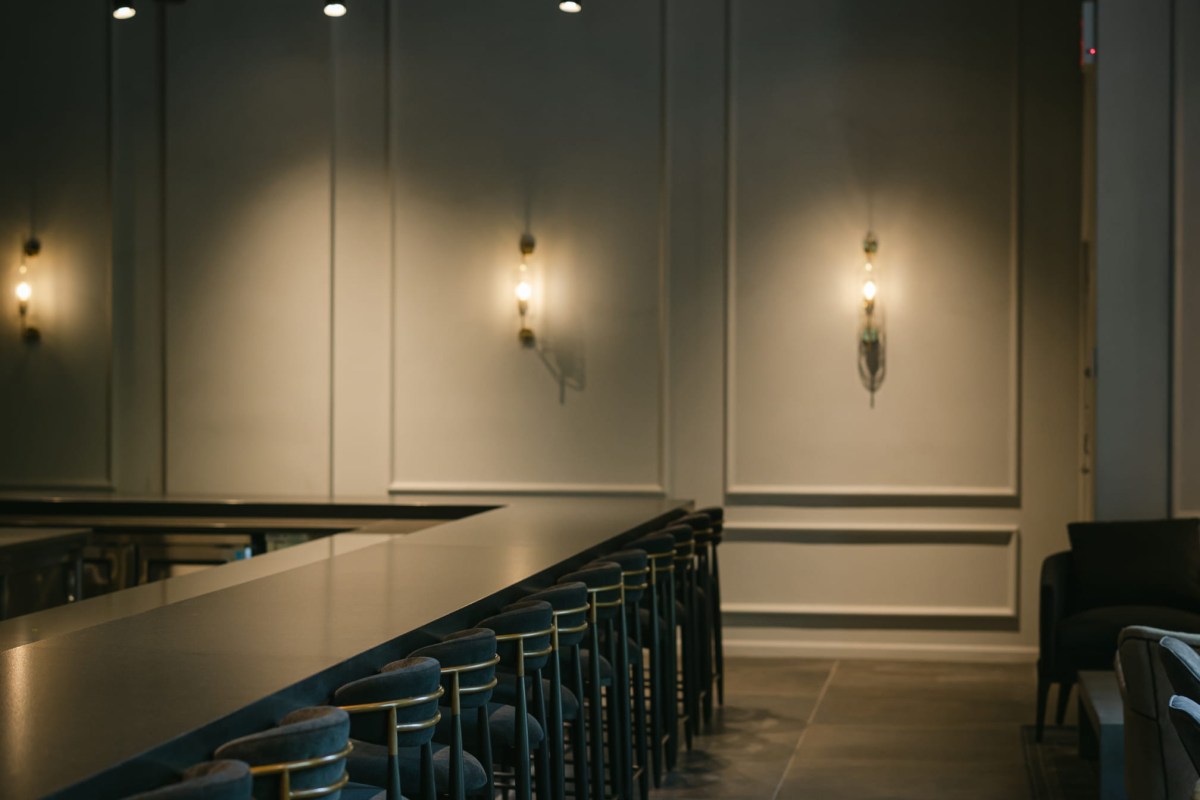 Bar area with velvet blue stools, long counter, and wall sconces in a dim, upscale interior