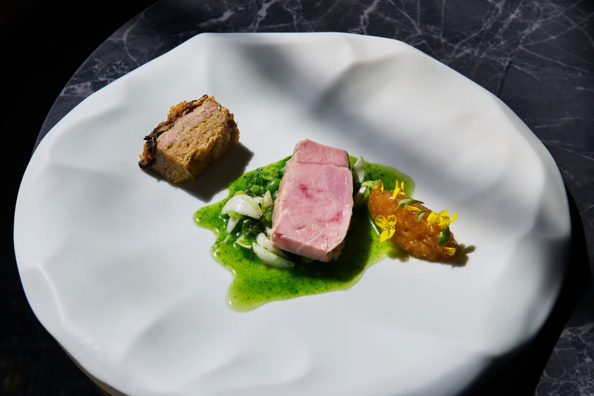 Elegant plated dish with sliced pork, pea puree, and citrus garnish on a white ceramic plate