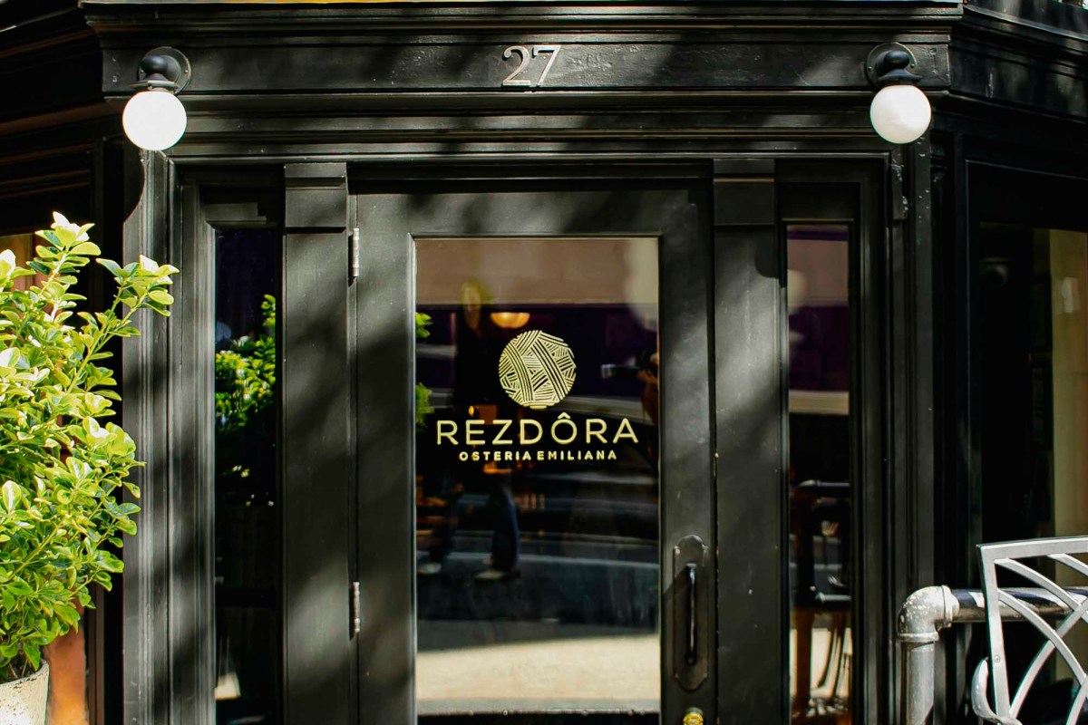Exterior entrance of Rezdôra with black-framed door and gold logo signage at 27
